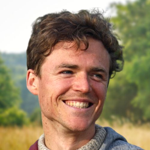 Porträt von Philip Kunisch, Mann mit dunklem lockigem Haar, lächelnd vor grünem Naturhintergrund