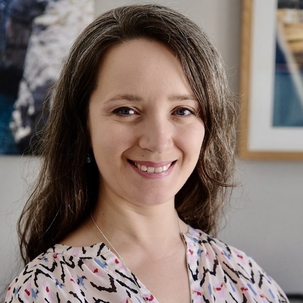 Tanja, dunkelhaarige Frau in gemustertem Oberteil vor Bürowand