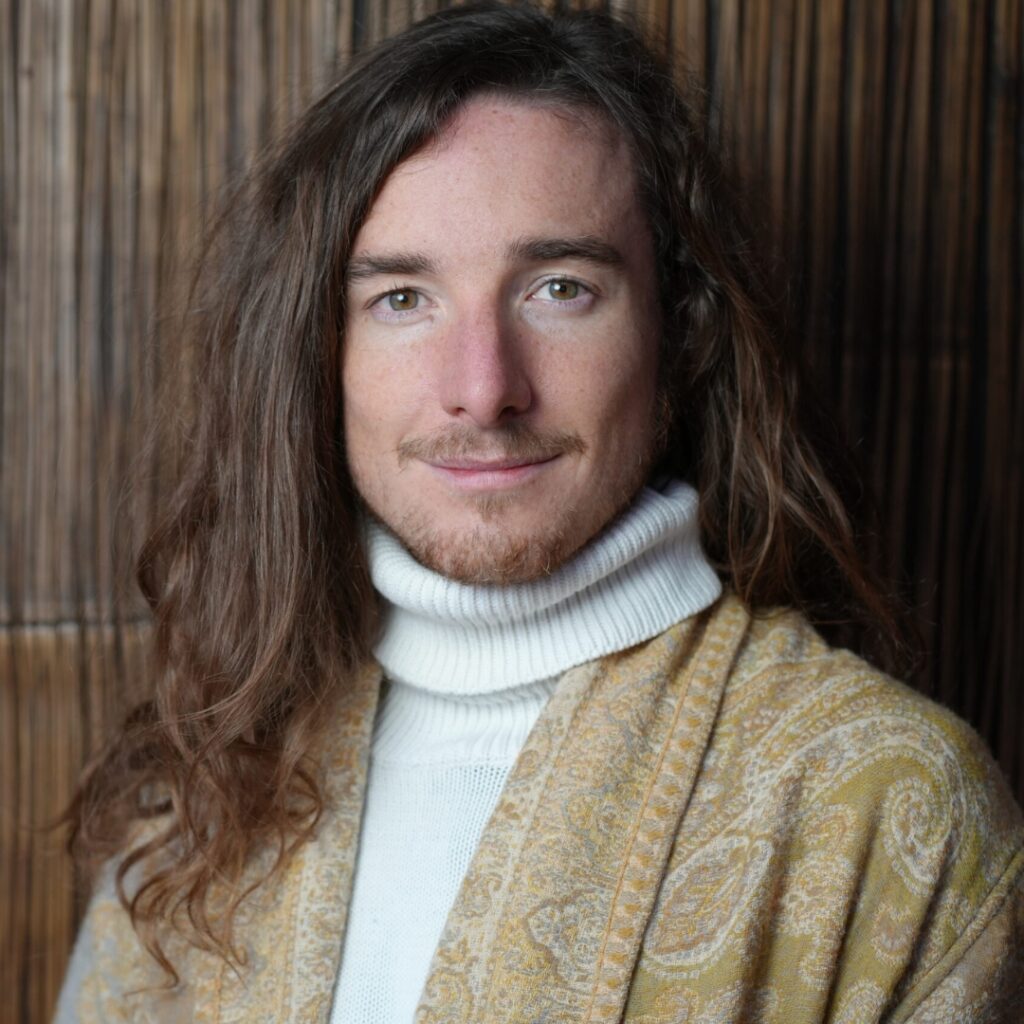 Robin Kaiser Porträt, lange dunkle Haare, weißer Rollkragenpullover, camel Cardigan, Holzwand im Hintergrund