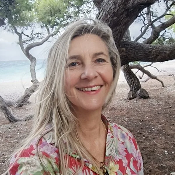 Porträt von Anna Roth, Frau mit schulterlangen glatten Haaren, lächelnd am Strand unter einem Baum