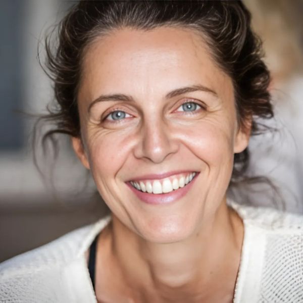 Frau mit dunklen Haaren hochgesteckt, weißem Pullover, strahlendes Lächeln, heller Hintergrund