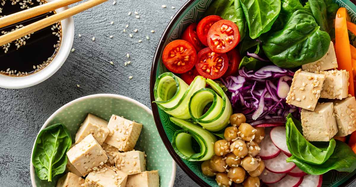 Vegane Schüsseln mit Tofu, Gemüse, Avocado und Sesamöl, Tischaufnahme