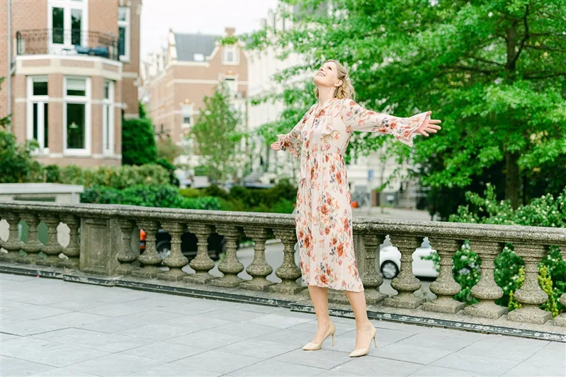 Sabine Walter in floralem Kleid mit ausgestreckten Armen vor historischem Balkon