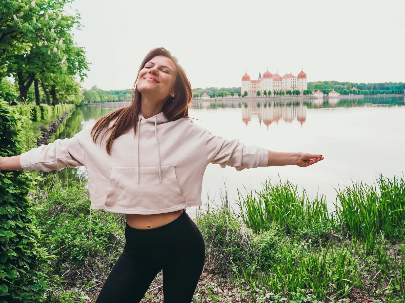 Dein Zyklus Guide – E-Book zur Periodenernährung von Jenny Tröger 4 Frau im Hoodie mit ausgebreiteten Armen vor Schloss am See