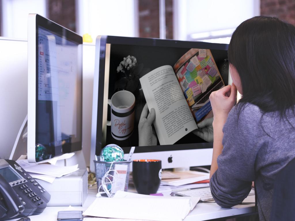Mockup: Frau sitzt am Schreibtisch vor iMac, liest offenes Buch mit farbigen Seiten