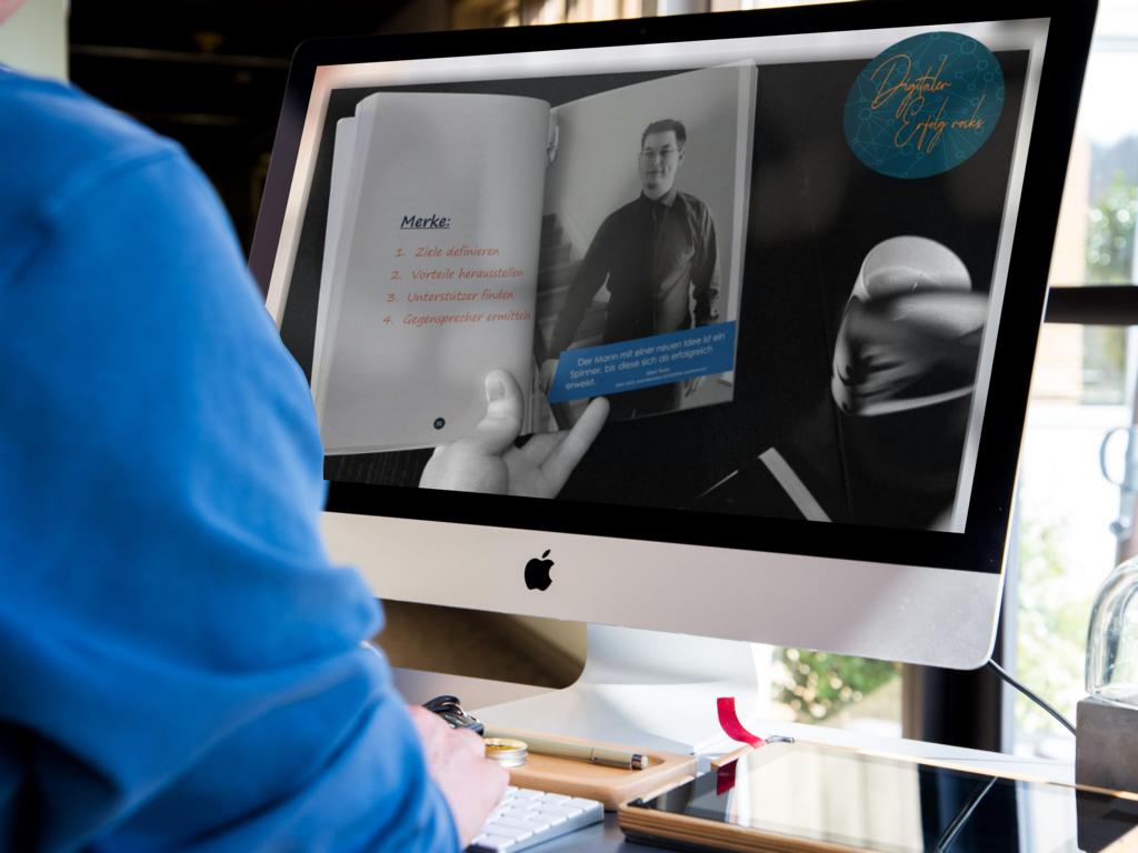 Mockup: Person liest Buch auf iMac-Monitor, zeigt innere Seite mit Merke-Liste und Porträt