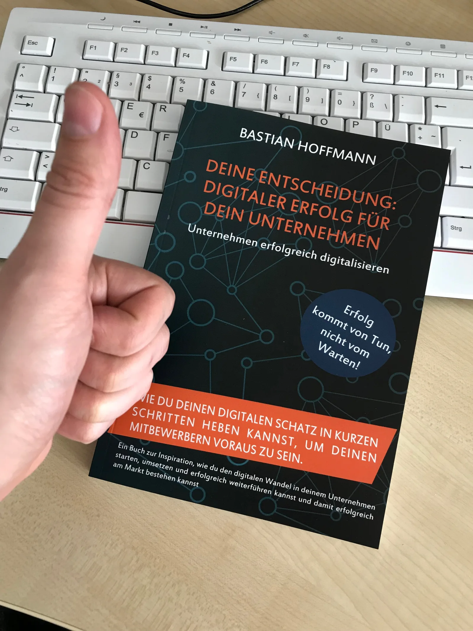 Hand hält Buch über Tastatur, Daumenhoch-Geste
