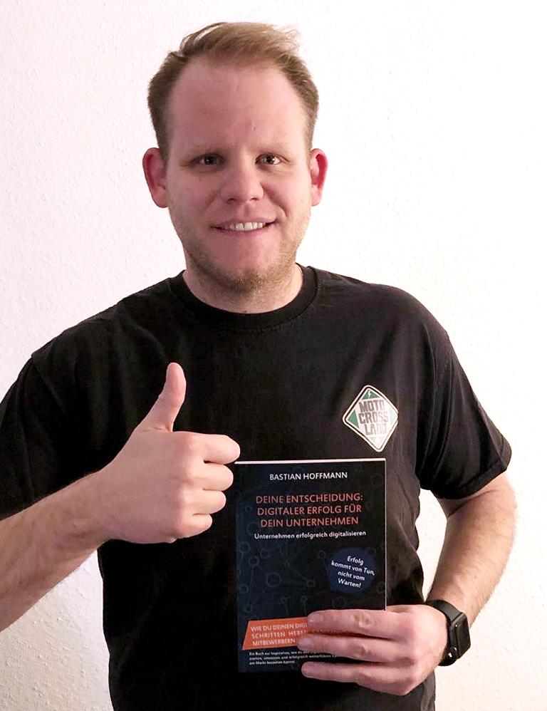 Mann im schwarzen Shirt mit Patch hält Buch und gibt Daumen-hoch-Zeichen