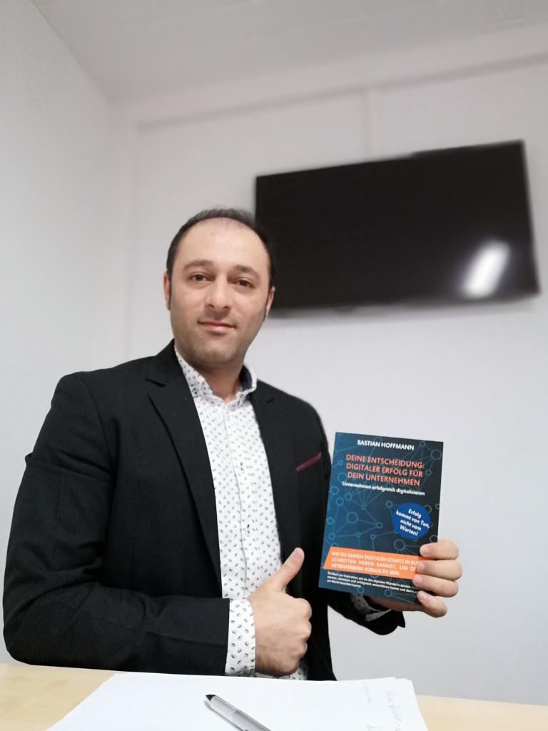 Mann im Anzug hält Buch und macht Daumen-hoch-Geste