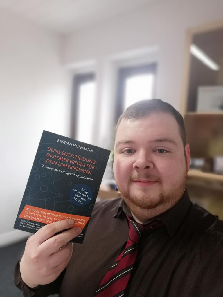Mann mittleren Alters hält Buchcover stolz in die Kamera