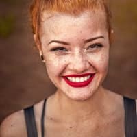 Porträtfoto einer Frau mit roten Haaren und rotem Lippenstift, lächelt in die Kamera