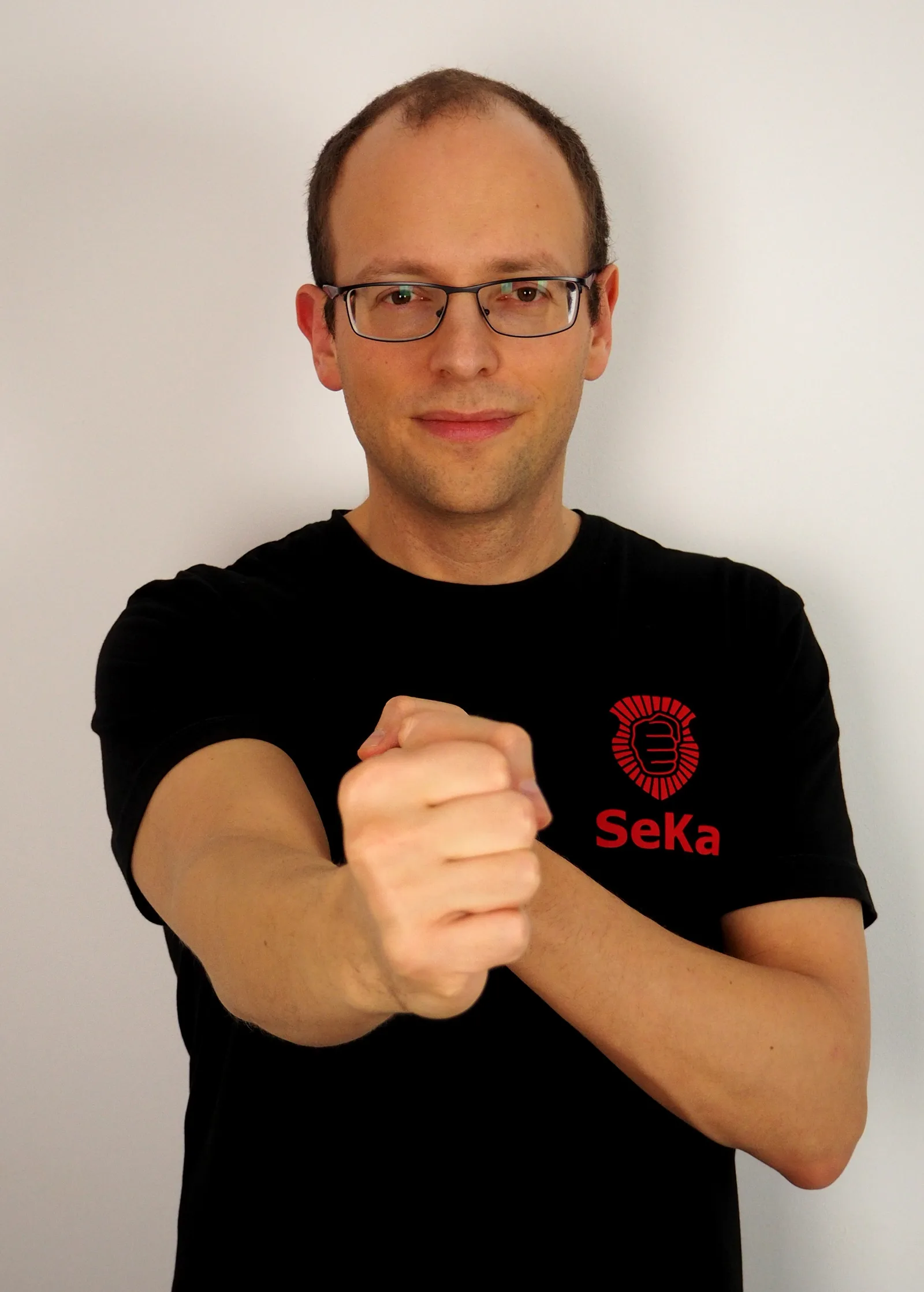 Mann mit Brille in schwarzem SeKa-Shirt demonstriert Kettenfauststoß-Grundposition frontal