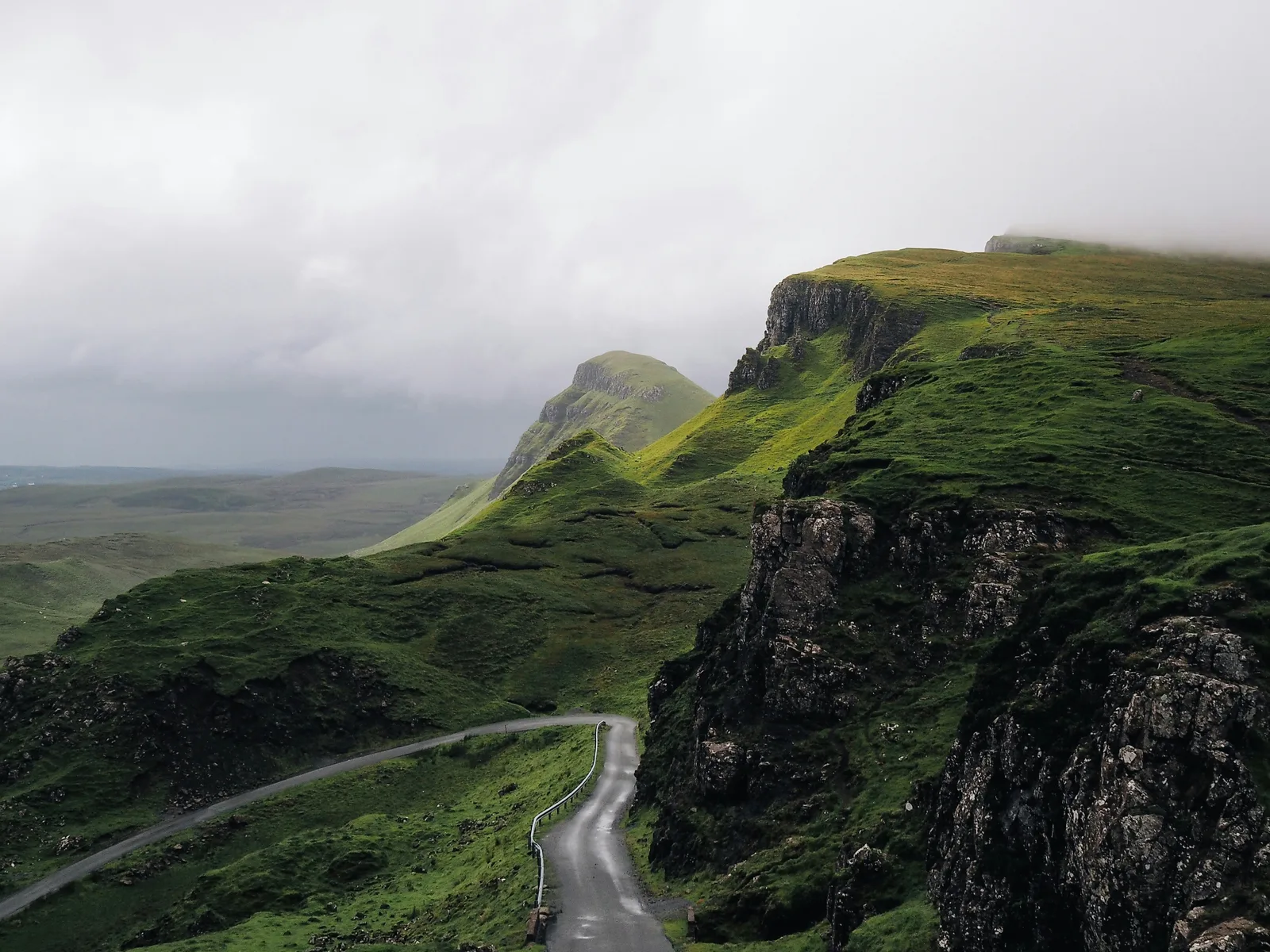 Berglandschaft mit grünen Hügeln, Felsen und Straße, neblige Atmosphäre