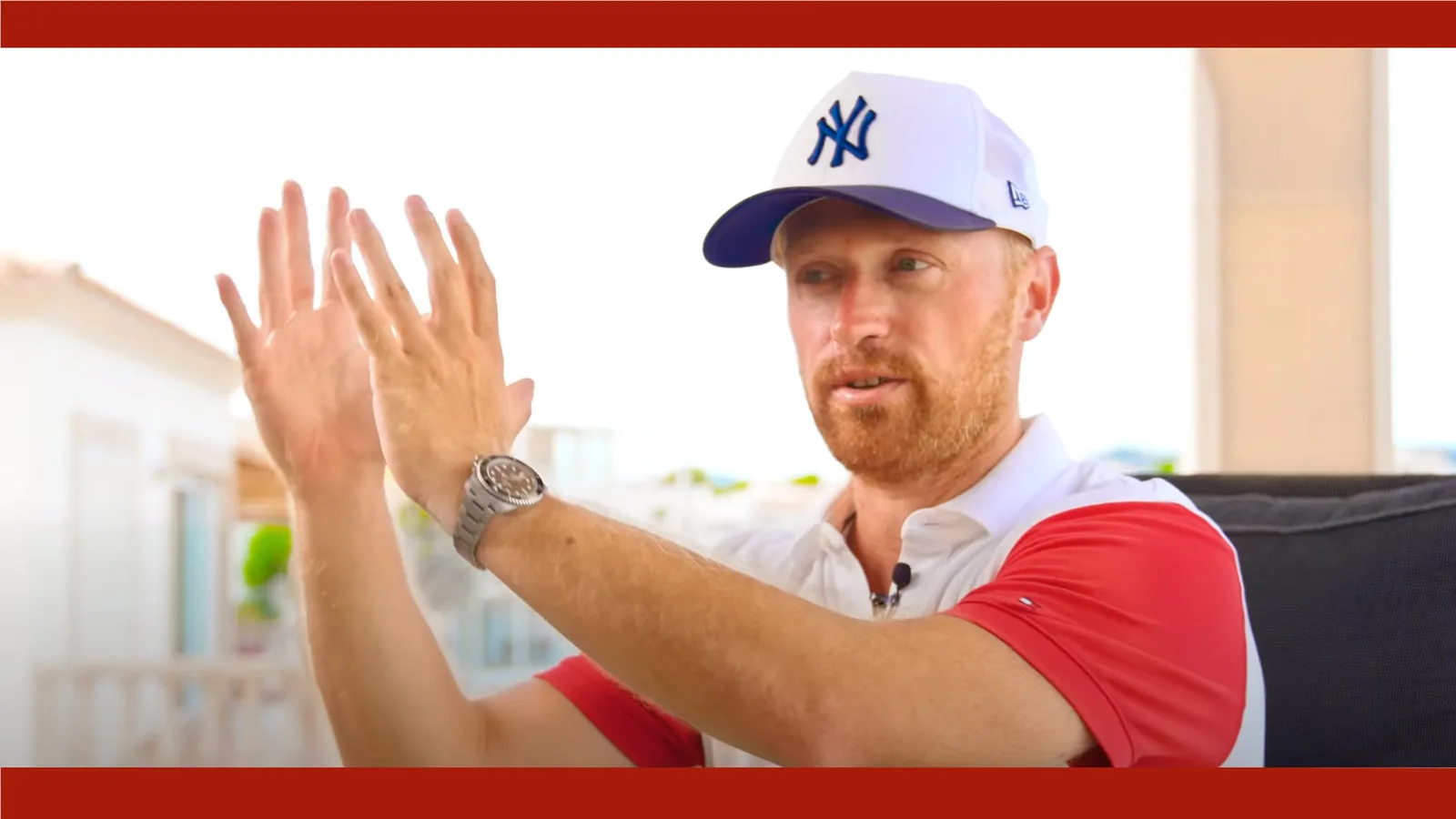 Danny Adams mit NY-Kappe clappend, weißes und rotes Shirt vor hellem Innenraum mit Play-Symbol
