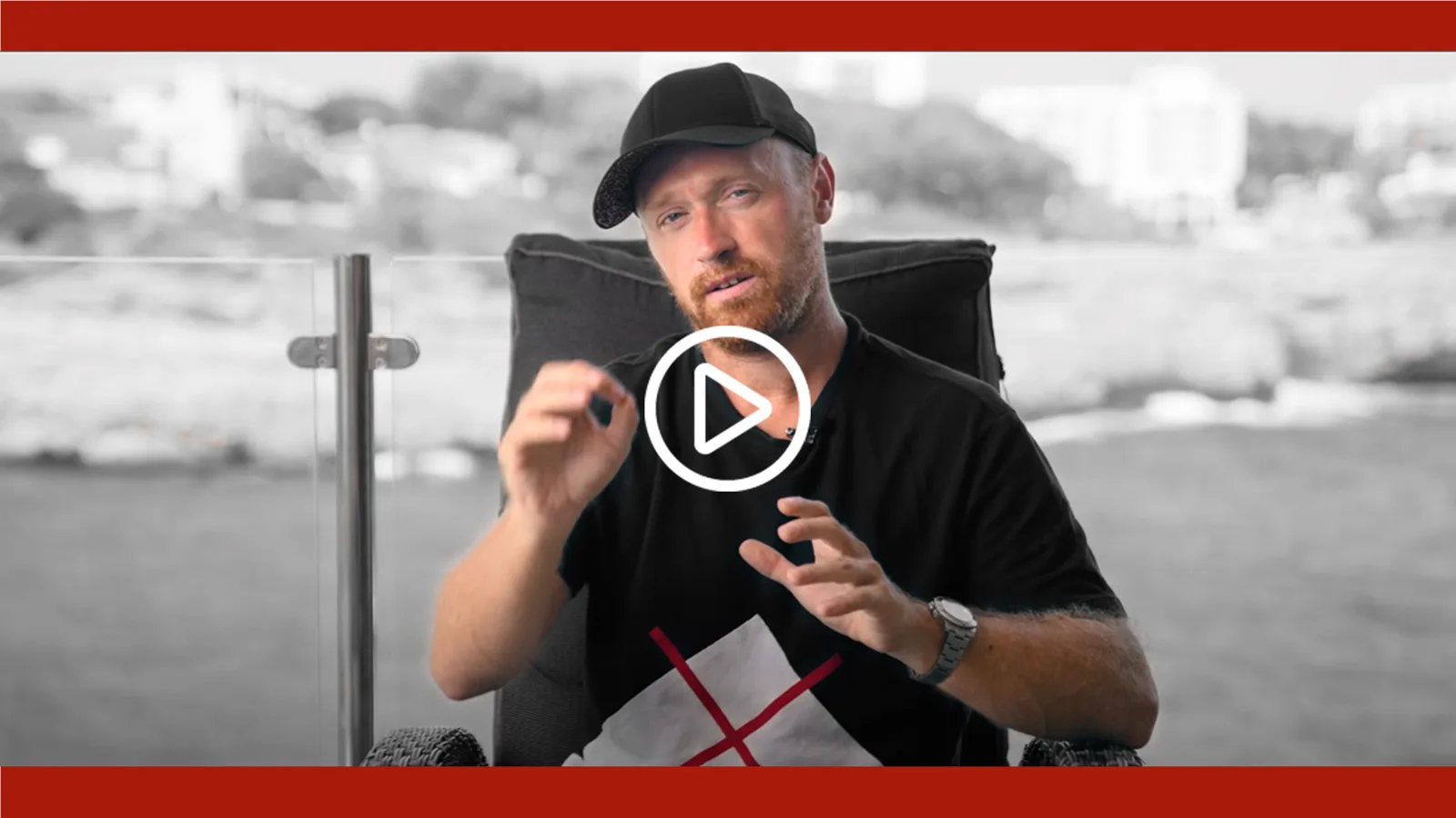Videostandbild von Danny Adams mit Baseballkappe am Wasser, gestikulierend mit Play-Symbol überlagert