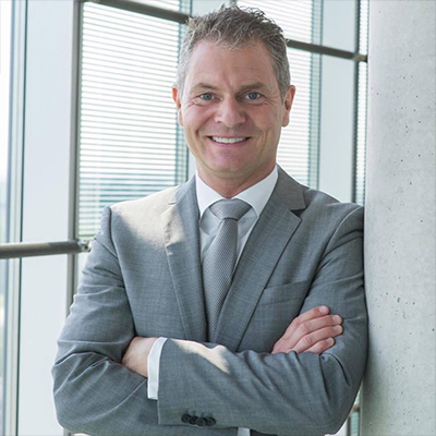 Dirk Kreuter, lächelnder Mann im grauen Anzug mit roter Krawatte vor Fenster