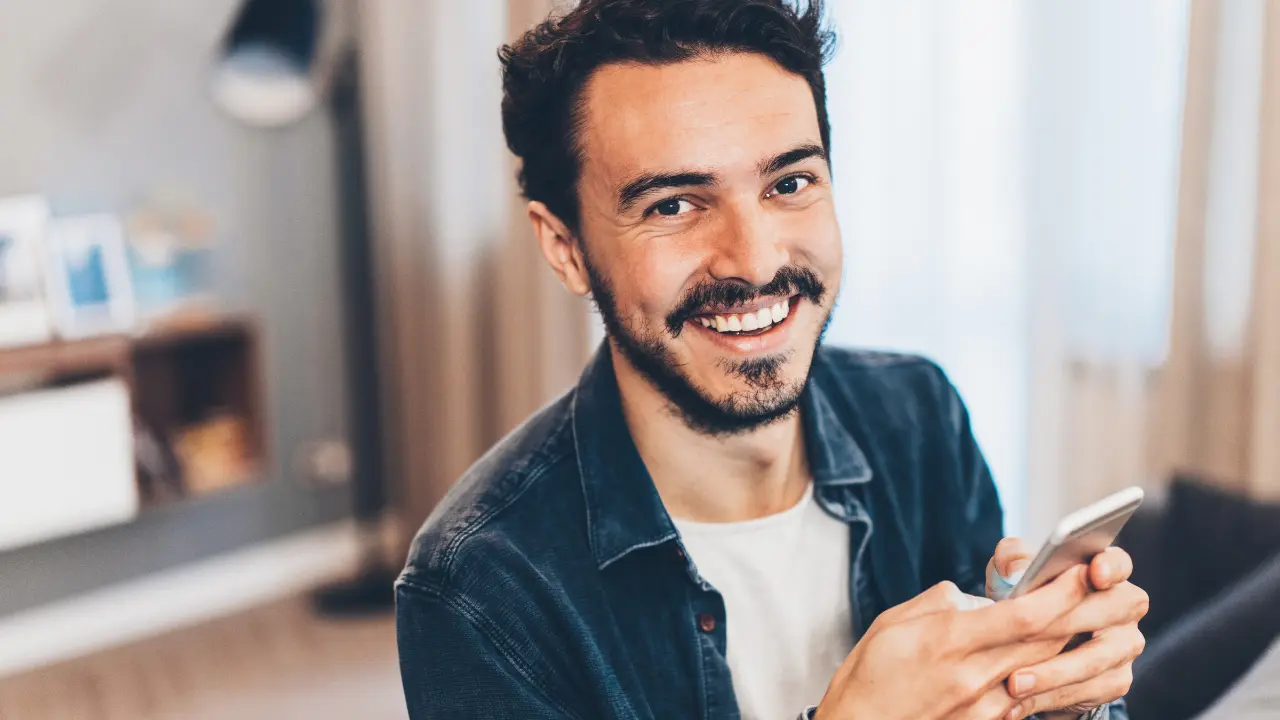 Mann mit Smartphone lächelt und hält Handy, Texting und Messaging Kontext
