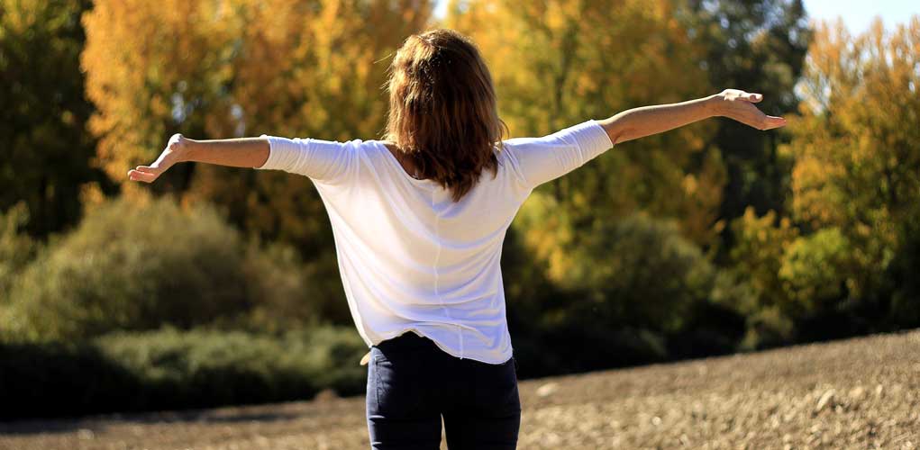 Frau mit ausgebreiteten Armen im weißen Shirt in herbstlicher Natur