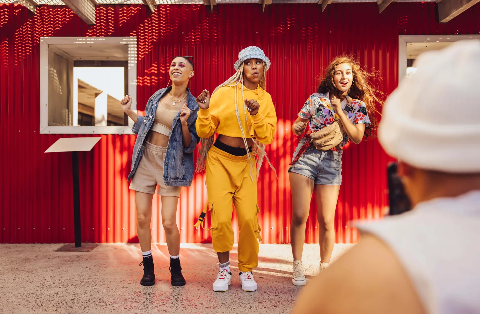 Drei junge Frauen tanzen vor roter Neon-Wand mit gelbem Outfit