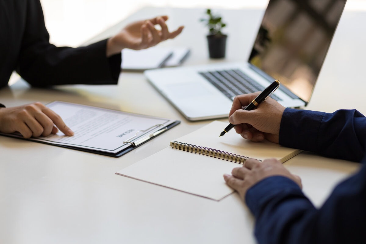 Zwei Personen arbeiten an Schreibtisch mit Laptop und Dokumenten