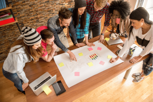 Gruppe von Personen bei Workshop-Aktivität mit farbigen Moderationskarten auf Holztisch