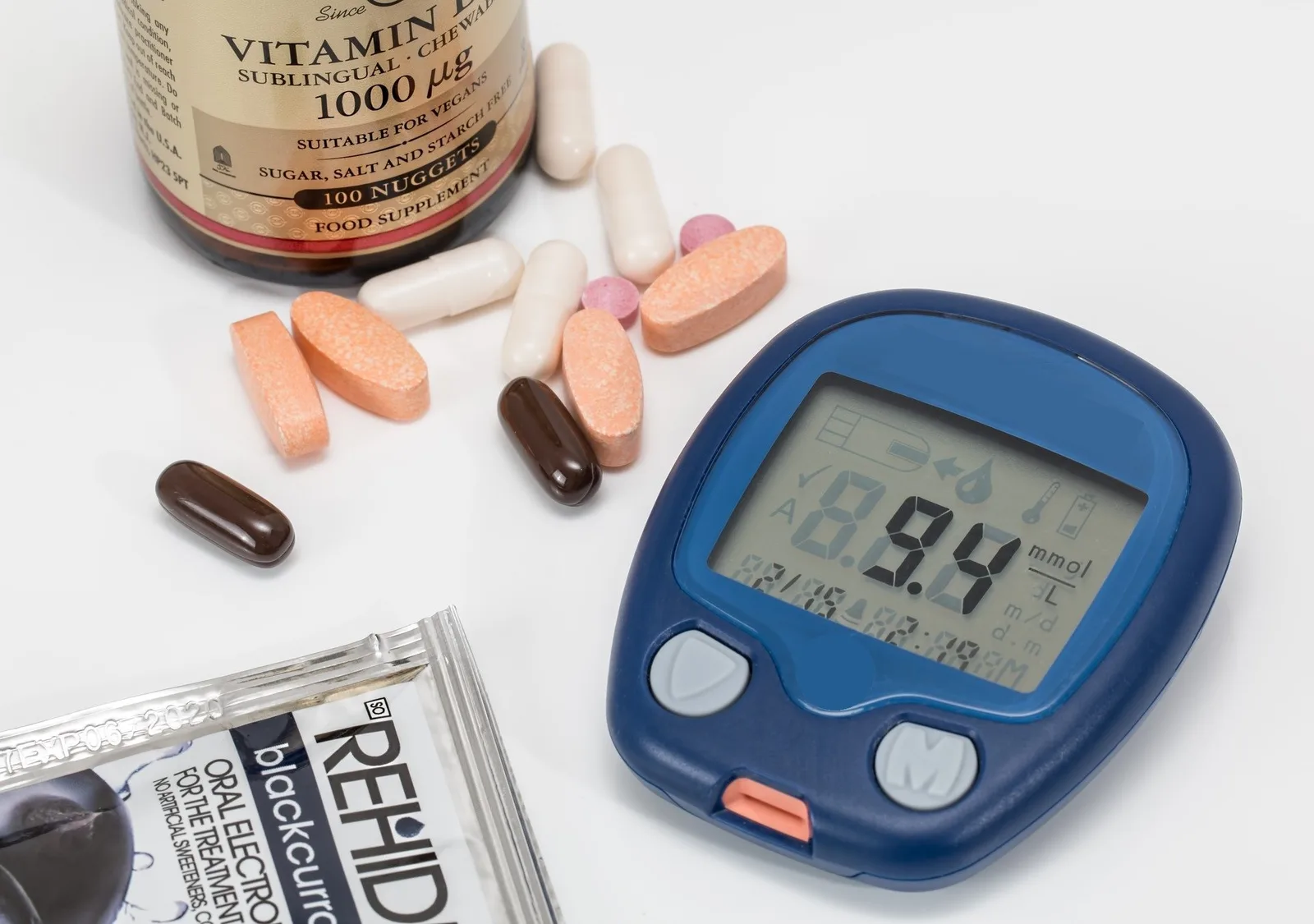 Blutzuckermessgerät mit digitaler Anzeige, Vitaminflaschen und Tabletten, Bluttest-Set auf weißem Hintergrund