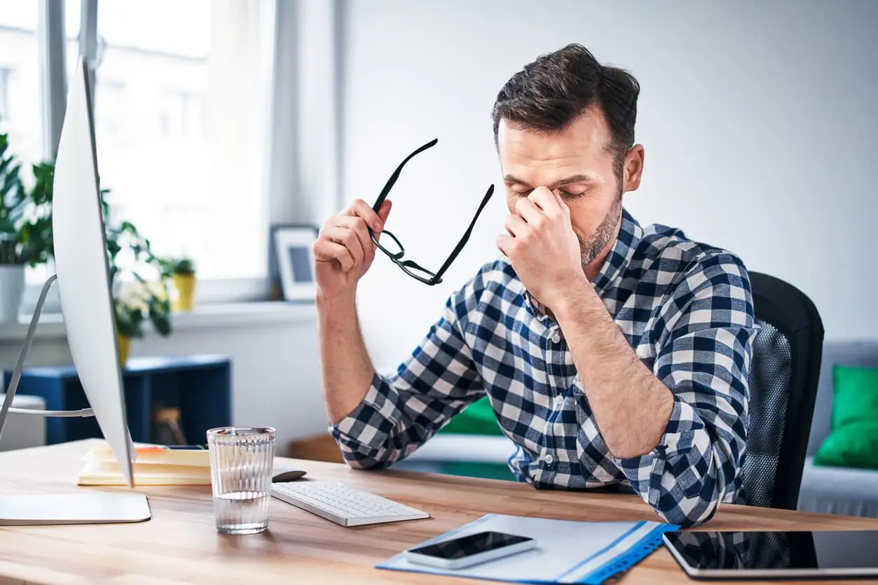 Mann am Schreibtisch mit Computer, hält Brille, wirkt konzentriert und nachdenklich