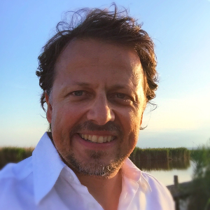 Porträt von Roland Hamm, lachender Mann mit Oberlippenbart vor Himmelshintergrund