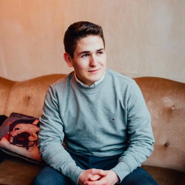 Junger Mann in grauem Pullover auf Sofa sitzend, Kundenstimme