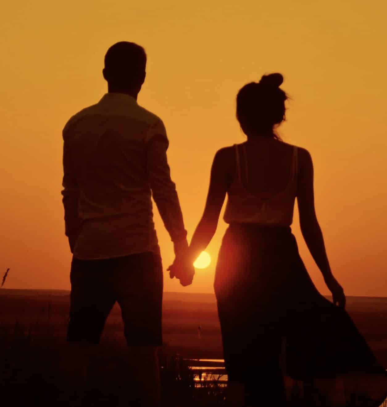Paar Hand in Hand vor goldenem Sonnenuntergang, beide Silhouetten