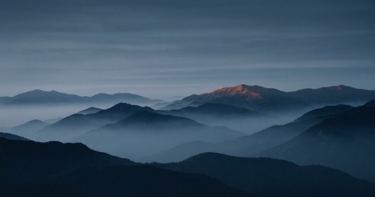 Berglandschaft mit mehreren Gebirgsketten im Nebel und blauem Himmel