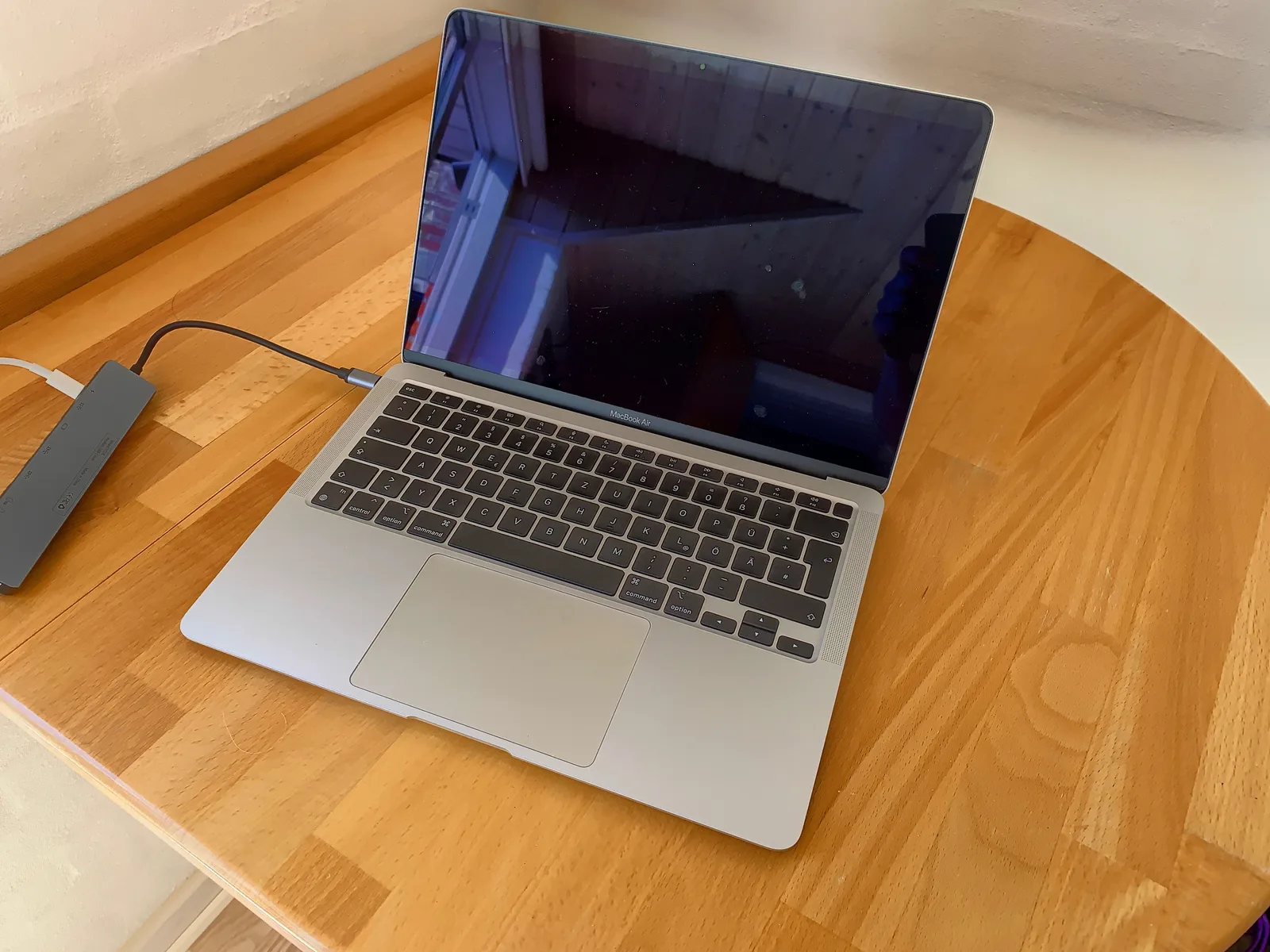 Silbernes MacBook auf Holztisch mit externem USB-C Hub und weißer Umgebung