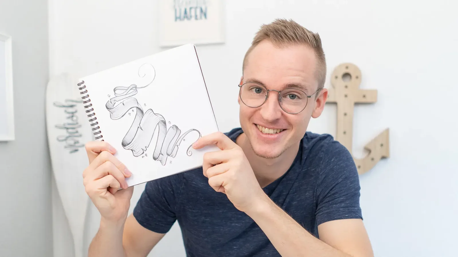 Man mit Brille zeigt Spiralblock mit Banner-Skizzen in Studio-Setting