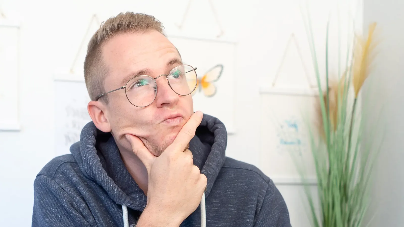 Man mit Brille in nachdenklicher Pose neben Banner-Designs an der Wand