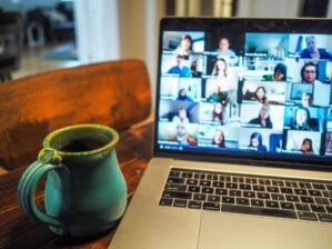 Laptop-Bildschirm mit Webinar-Teilnehmern in Videokonferenz, Kaffeetasse auf Holztisch