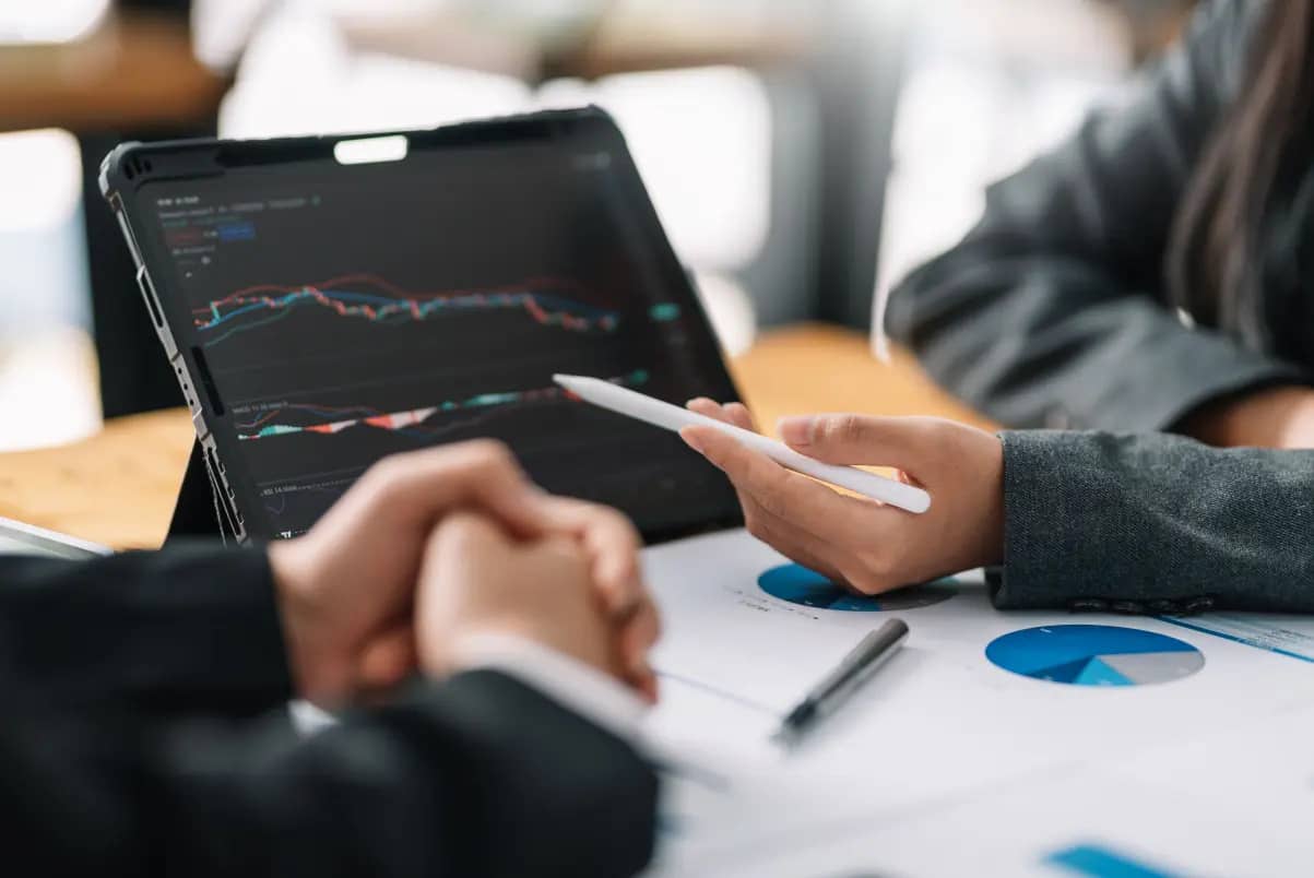 Zwei Personen analysieren Finanzdiagramme auf Tablet mit Anlagedaten