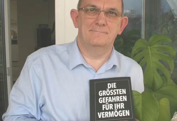 Mann in hellblauem Hemd mit Brille hält Buch "Die größten Gefahren für Ihr Vermögen"