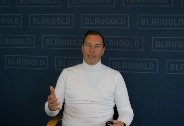 Mann in hellblauem Hemd mit Brille vor BLAUGOLD-Hintergrund