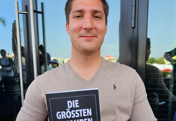 Junger Mann in Graumeliert-Shirt hält Buch "Die größten Gefahren für Ihr Vermögen"