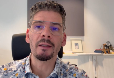 Junger Mann mit blauer Brille spricht zu Kamera, Nahaufnahme