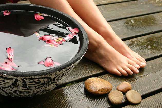 Frauenfüße in einer schwarzen Schale mit Wasser, rosafarbenen Blütenblättern und Steinen