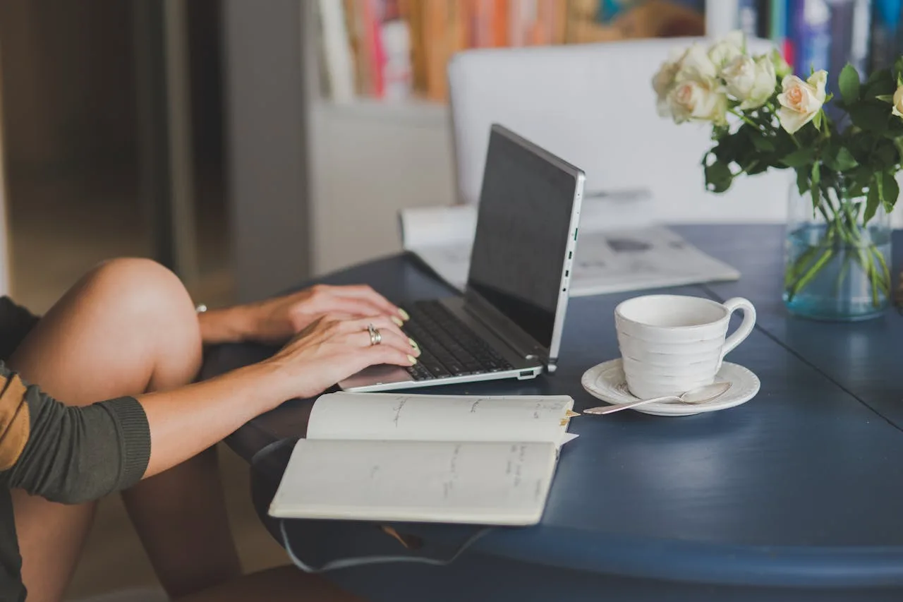 Frau arbeitet am Laptop mit Kaffee und Blumen im Home-Office
