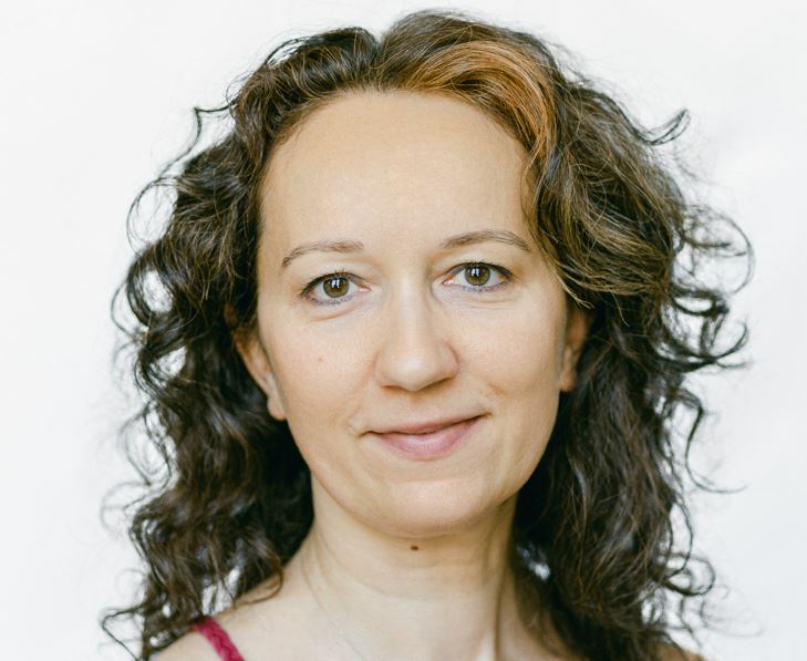 Kopfportrait einer Frau mit lockigen braunen Haaren, rosa Top, vor hellem Hintergrund