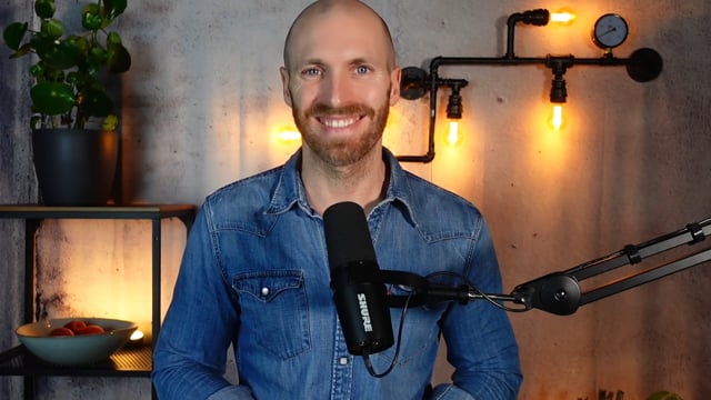 Michael Asshauer im Podcast-Studio mit Mikrofon, blauem Jeanshemd und warmem Licht