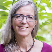 Portraitfoto: Ältere Frau mit grauem Haar, Brille und lila-orangefarbenem Top, lächelnd