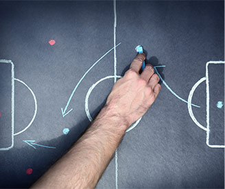 Hand zeichnet Fußball-Taktik auf Kreidetafel mit Spielfeld und Pfeilen