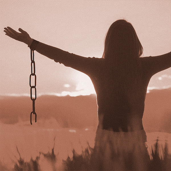 Silhouette einer Frau mit ausgebreiteten Armen, die eine Kette fallen lässt, symbolisiert Befreiung und Verzeihen