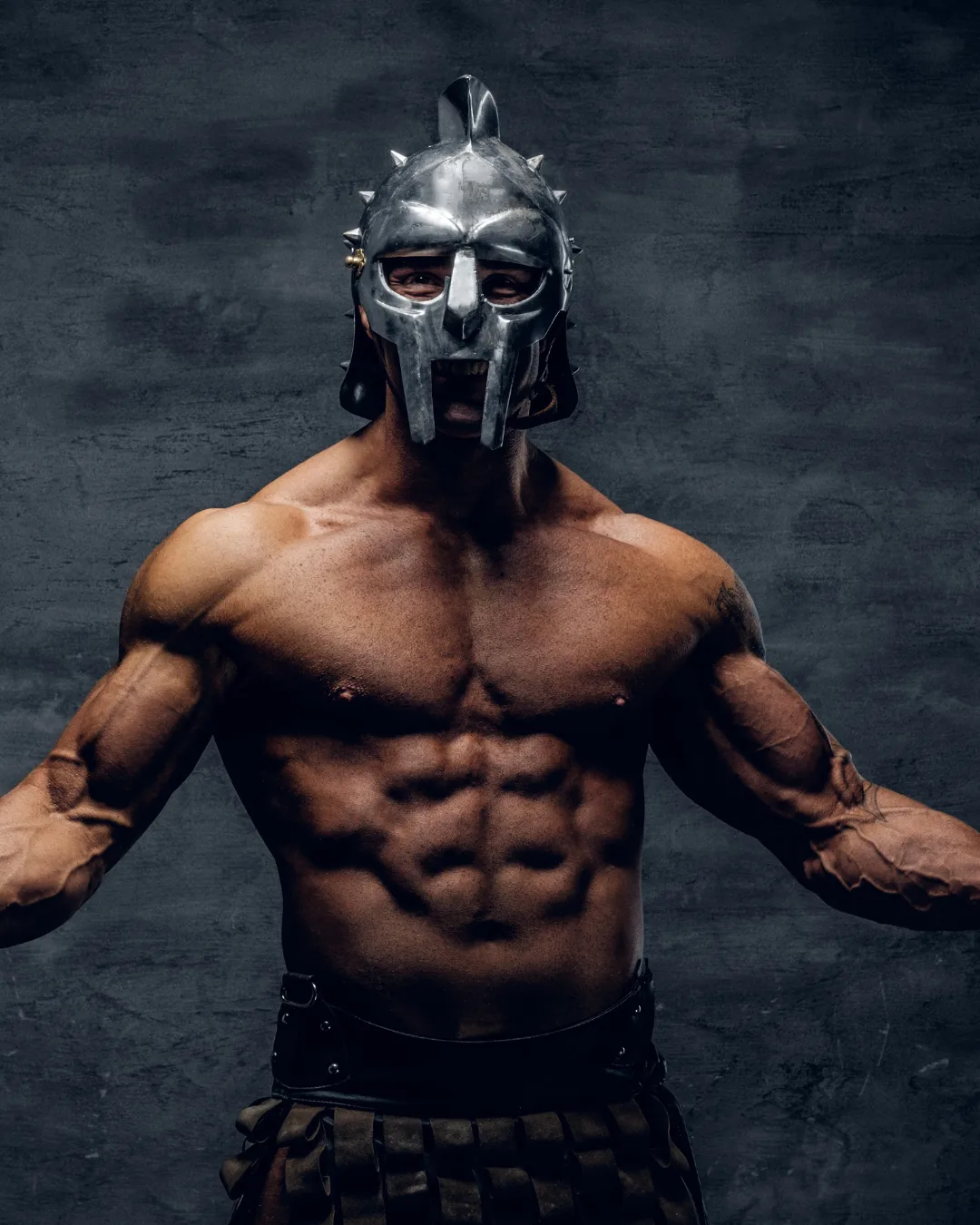 Muskulöser Mann mit Gladiator-Helm und Schulterpanzer, definierte Bauchmuskeln vor grauem Hintergrund