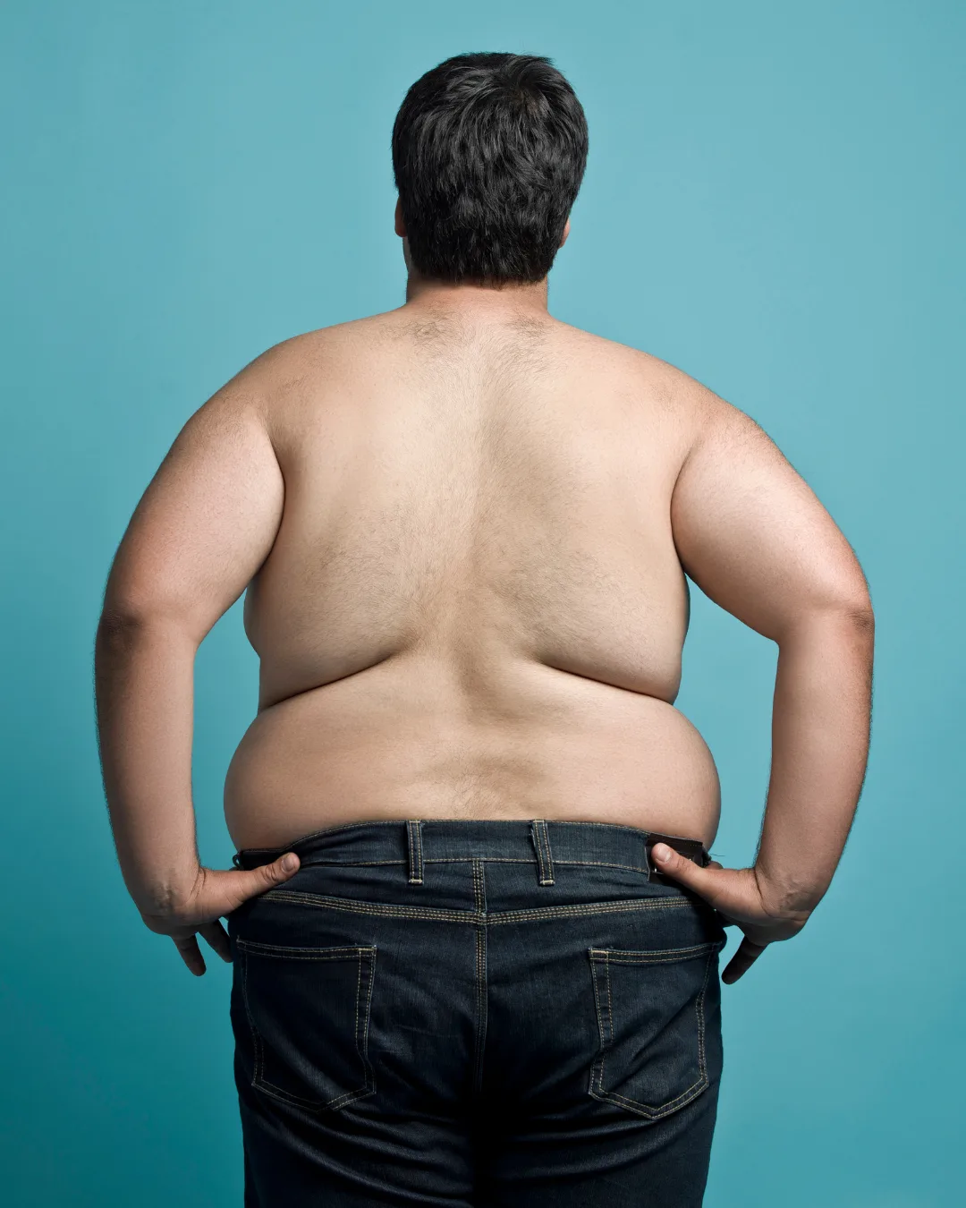 Mann von hinten mit erhöhtem Körpergewicht, blauer Hintergrund, zeigt Vorher-Zustand für Body-Transformation