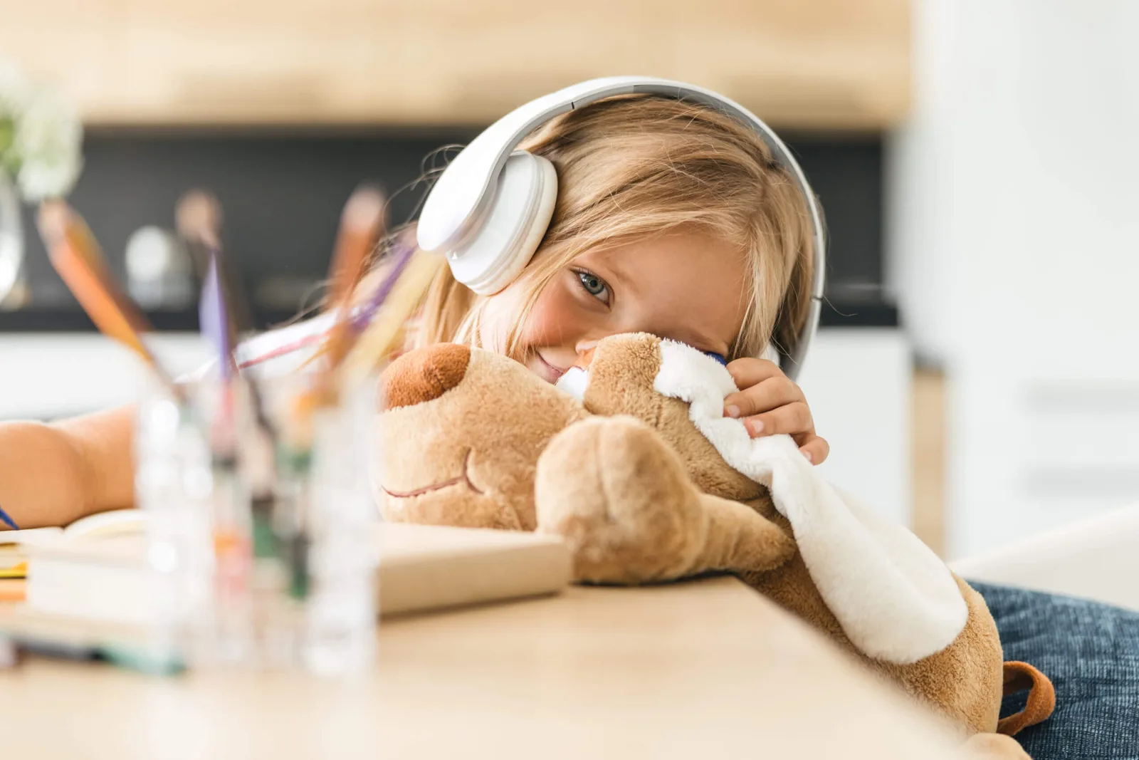 Kind mit Kopfhörern hält Teddybär, sitzt am Schreibtisch beim Hören